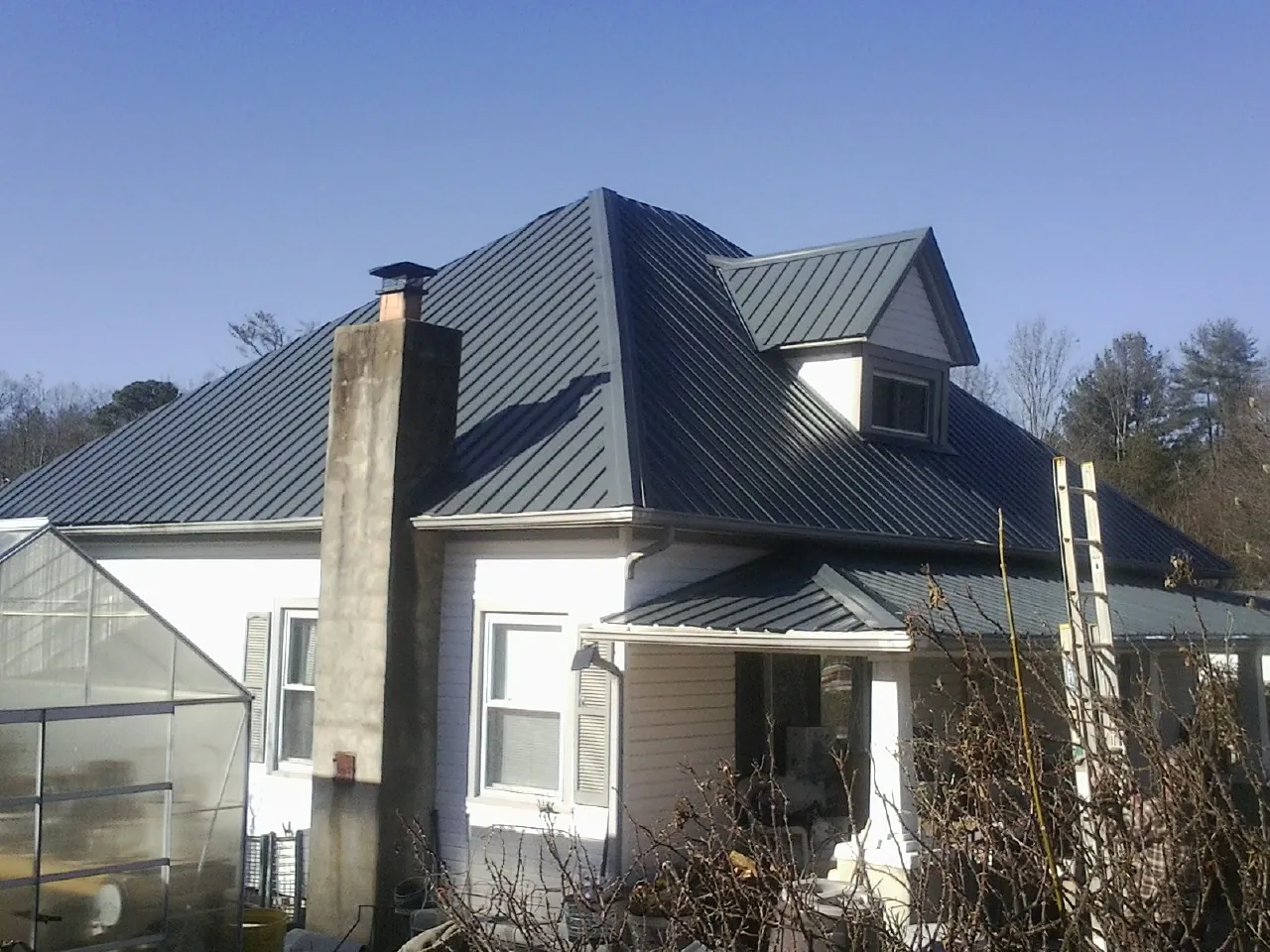 Dark blue standing seam metal roof on a white farmhouse with dormer — Slate & Tile Roof Repair by Roofing Brothers in Allen Park