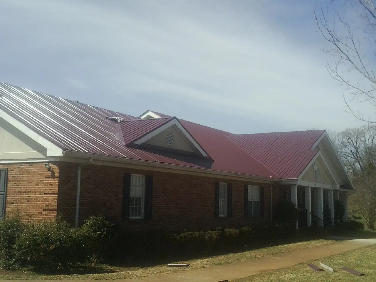 Red metal roof with gabled entries on a long brick building, from a Hail Damage Roof Repair job in Allen Park