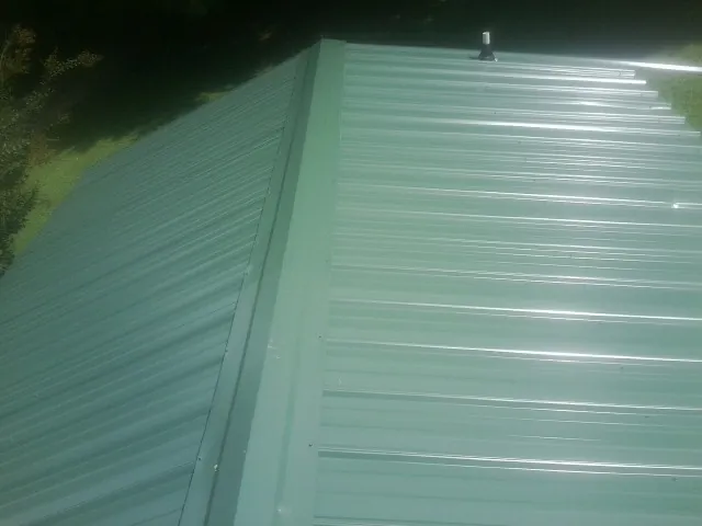 New green metal panels meeting at the ridge of a roof — Flat Roof Repair work by our crew in Allen Park