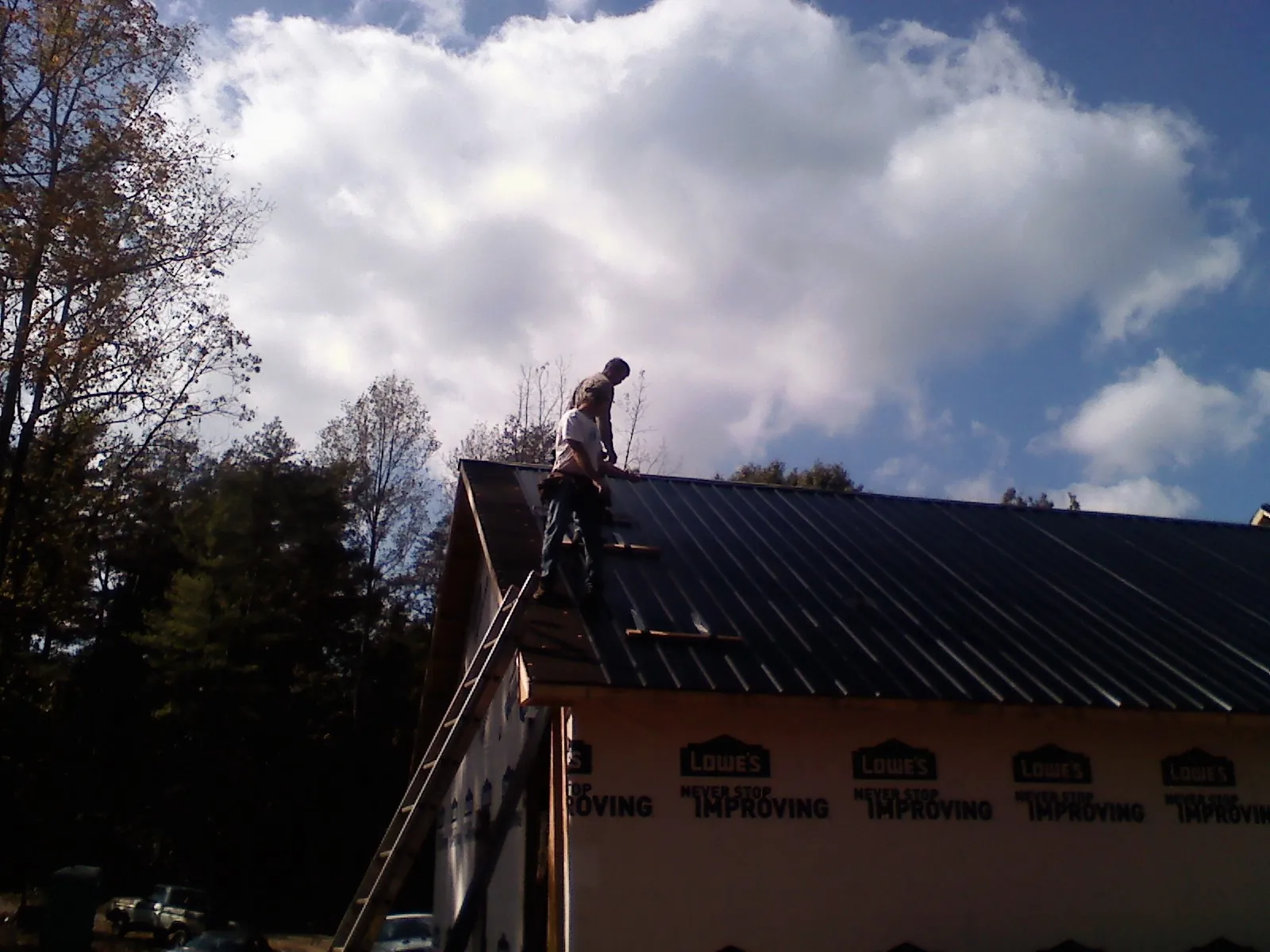 Roofer fastening dark metal panels high against a cloudy sky, from a Roof Inspection job in Allen Park