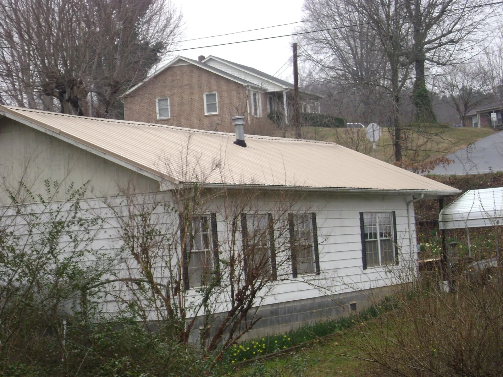Tan metal roof on a white sided house set into a hillside — Commercial Roofing by Roofing Brothers in Allen Park